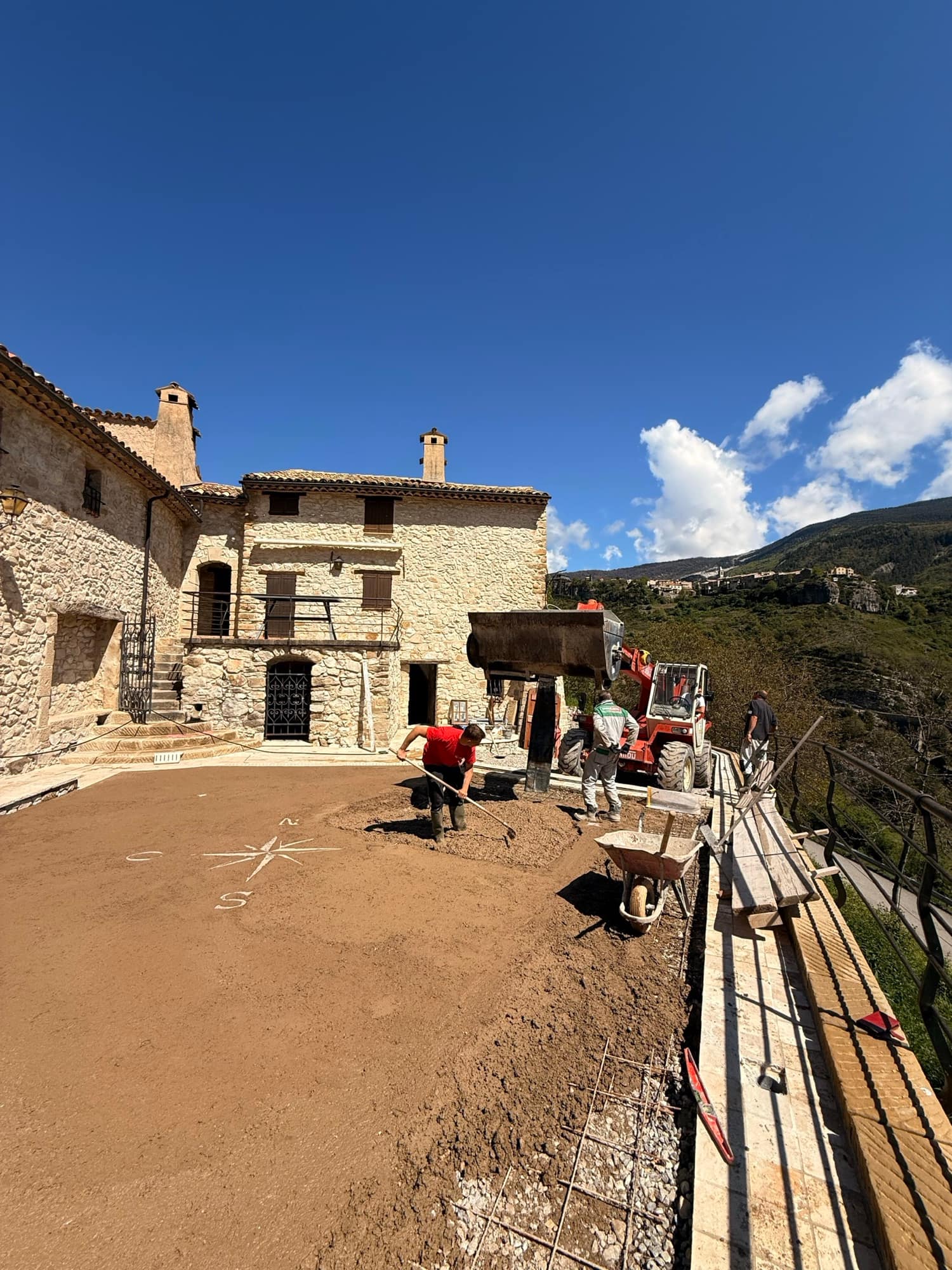 Coulage et réglage d'une dalle dans la cour d'une bâtisse en pierre, chariot télescopique et brouette sur le chantier.